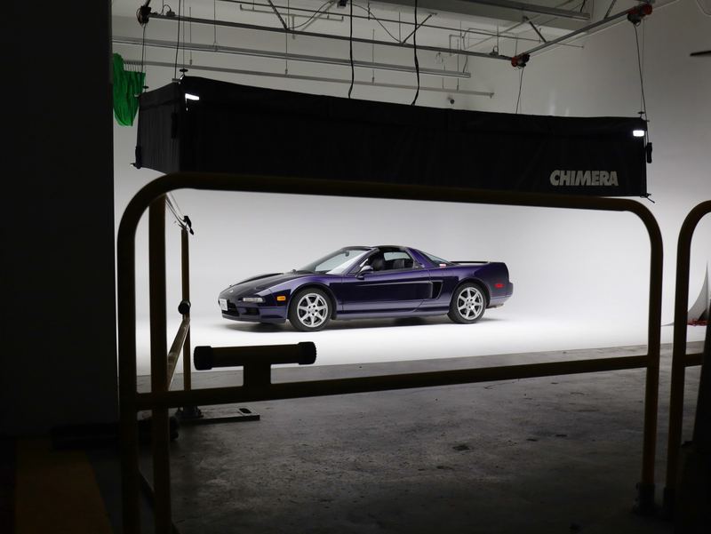 Behind the scenes: the purple NSX-T on a white cyclorama seen through a yellow safety railing, with a Chimera softbox overhead