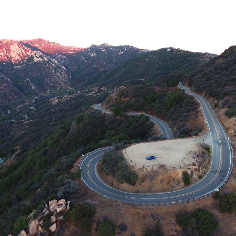 Aerial view of a winding mountain road with a hairpin turn and a parked car in the pullout