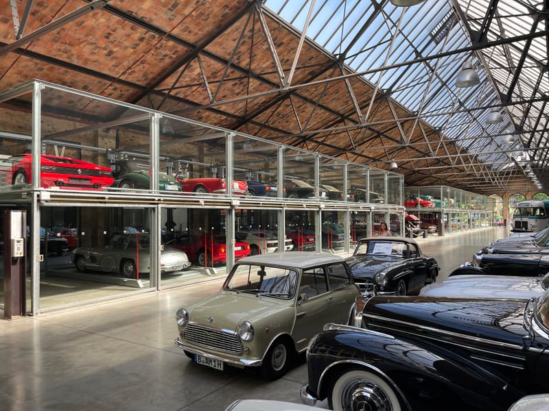Indoor car storage hall with classic cars on racks under a glass-and-steel roof
