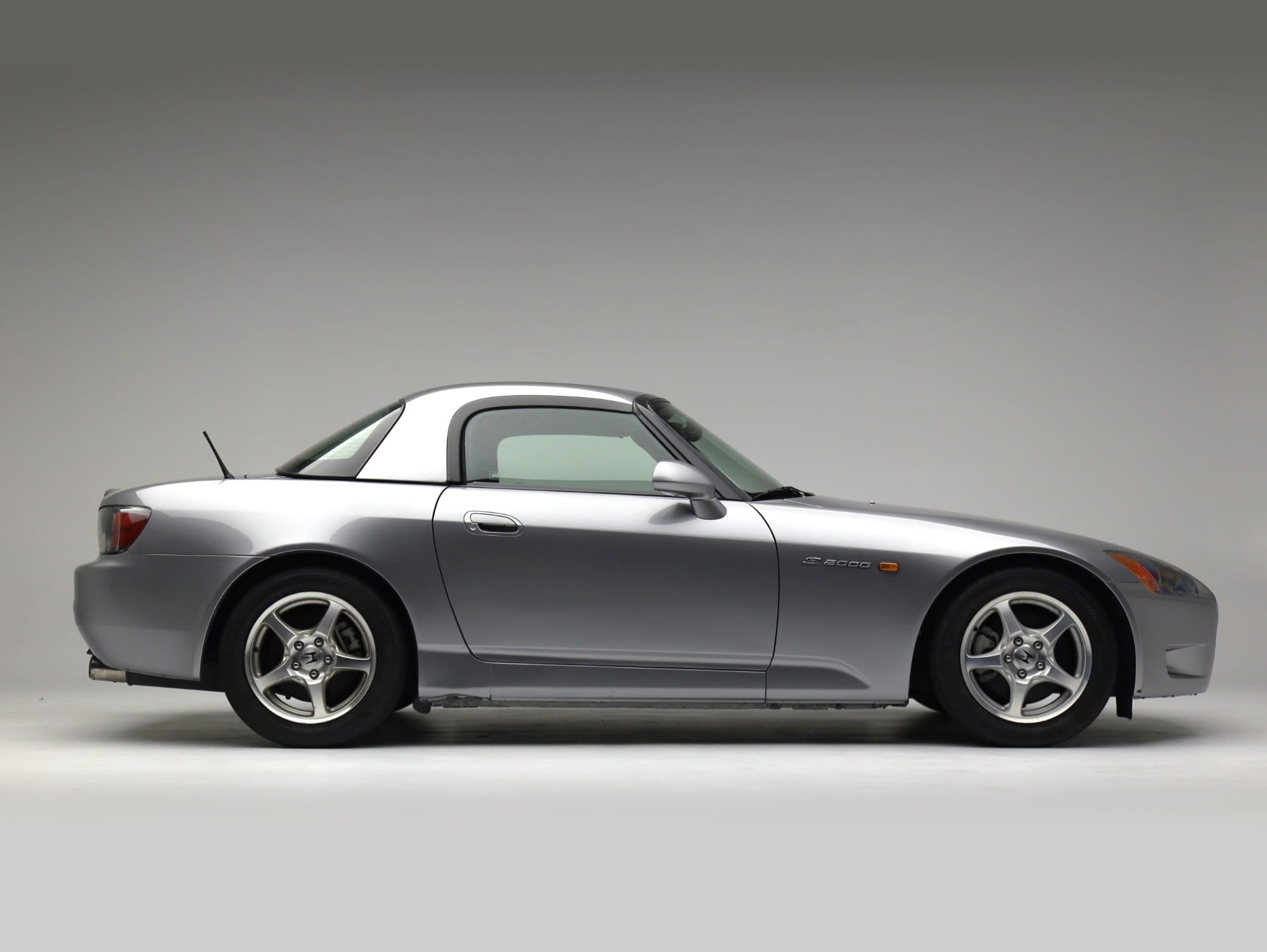 Silver Honda S2000 with hardtop, side profile on a gray studio backdrop