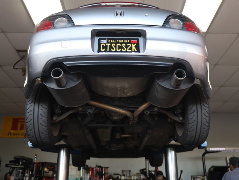 Underbody and dual exhaust of the silver Honda S2000 on a lift in a shop