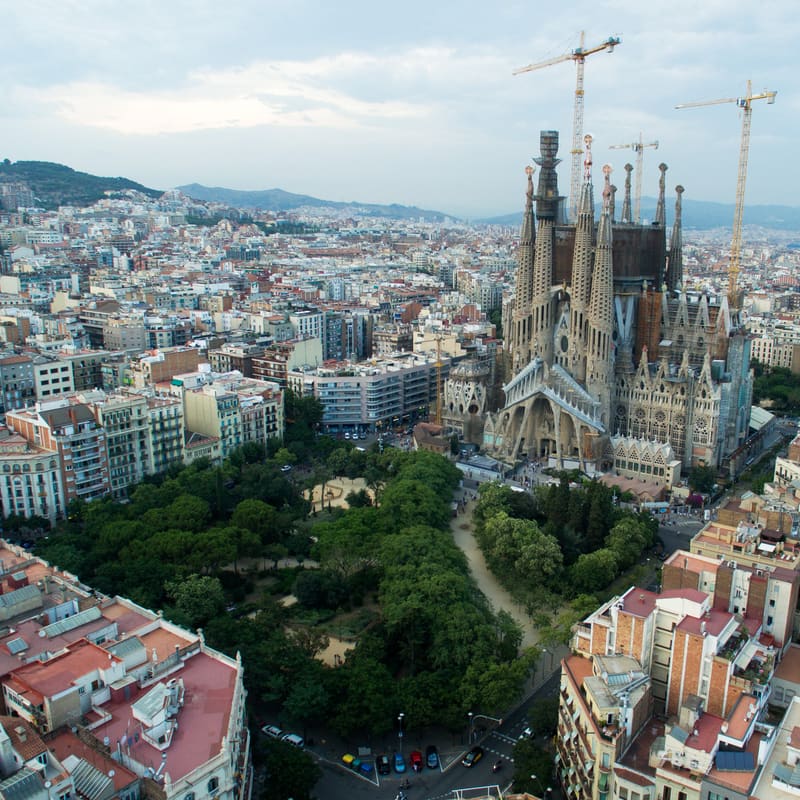 Aerial view of the Sagrada Família rising above the surrounding city blocks, with construction cranes