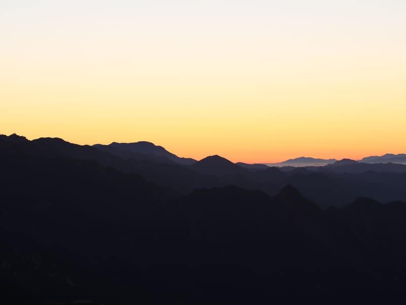 Silhouetted mountain ridges in the Sierra under an orange sunset sky