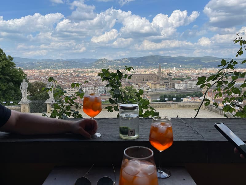 Three orange spritz cocktails on a terrace ledge overlooking a city and distant hills