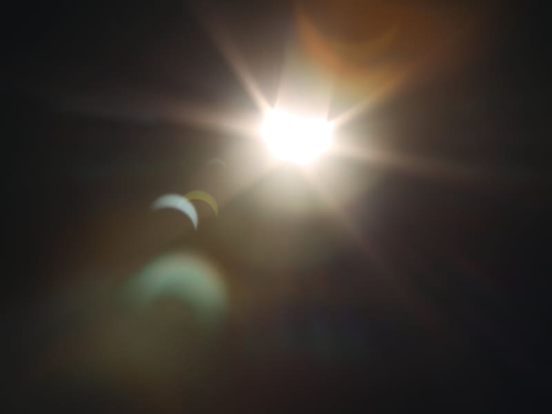 Partial solar eclipse with a bright starburst sun and crescent-shaped lens flares against a dark sky