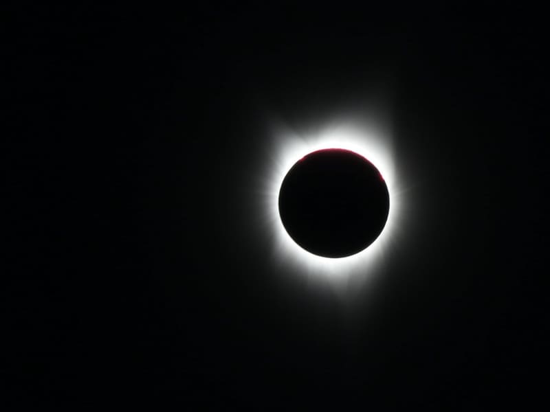 Total solar eclipse with the white corona around the black moon and a thin red prominence at the top edge